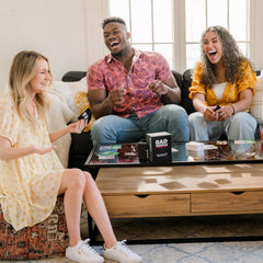 Friends laughing around a table during a BAD PEOPLE round for social fun.