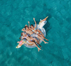 Two friends enjoy the PoolCandy Gigantic Unicorn raft on a lake.