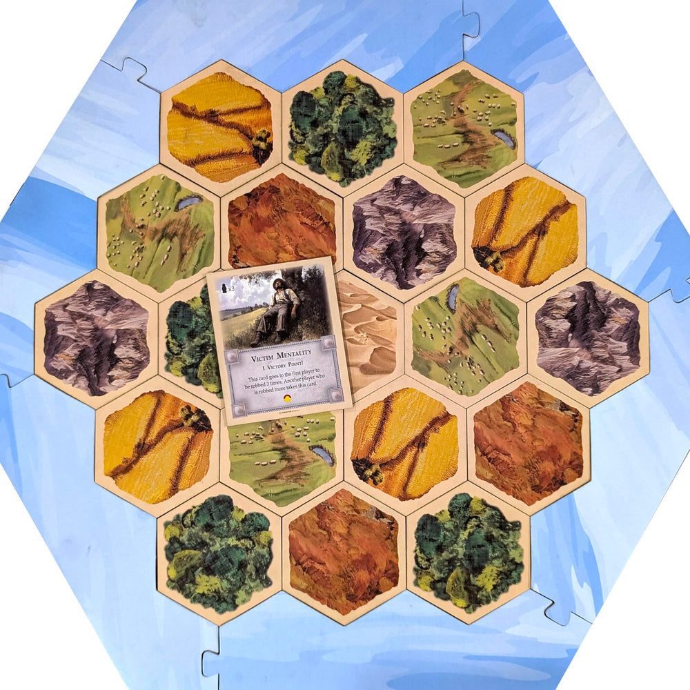 Tabletop Monthly Victim Mentality Card with Catan board, shows matching thickness and fit.