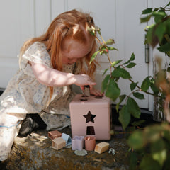 Mushie Shape Sorting Box Petal supports fine motor skill development.