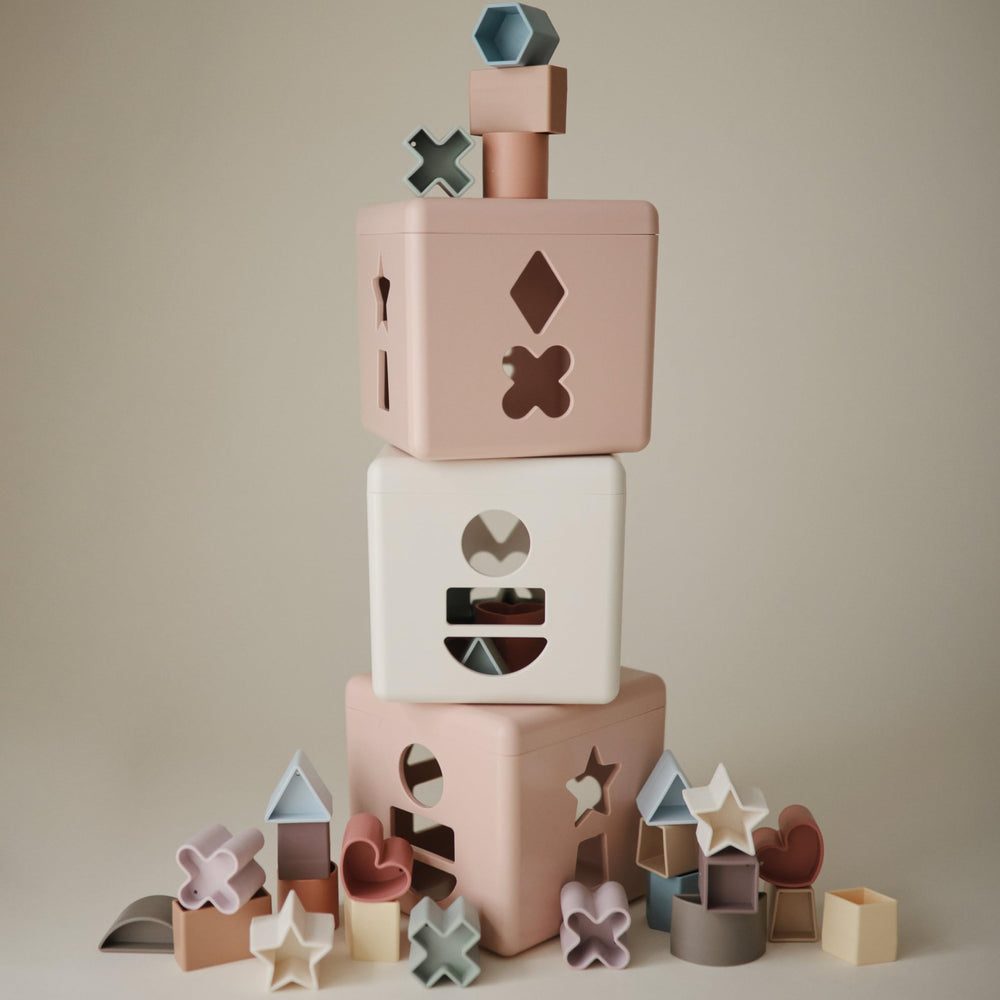 Mushie Shape Sorting Box Petal in soft colors enhances cognitive play.
