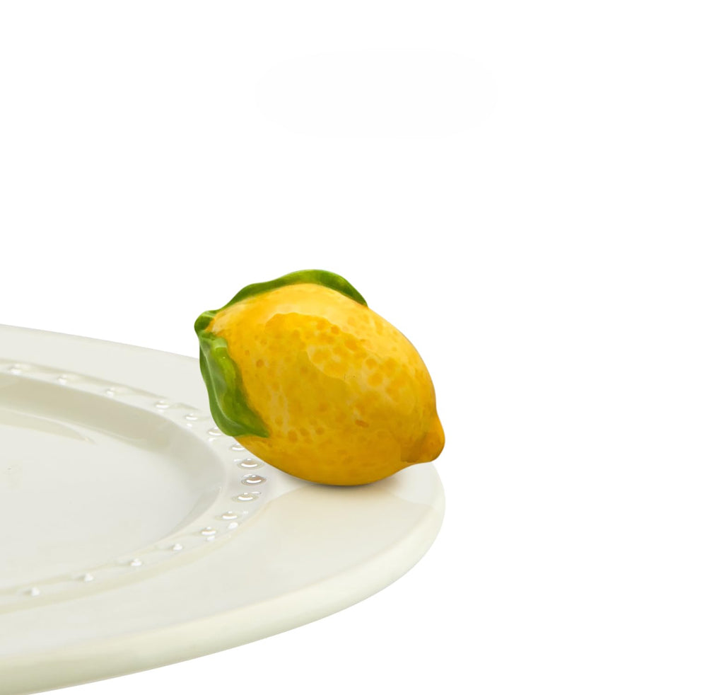 Nora Fleming Lemon Squeeze mini shines on a base for seasonal decor.