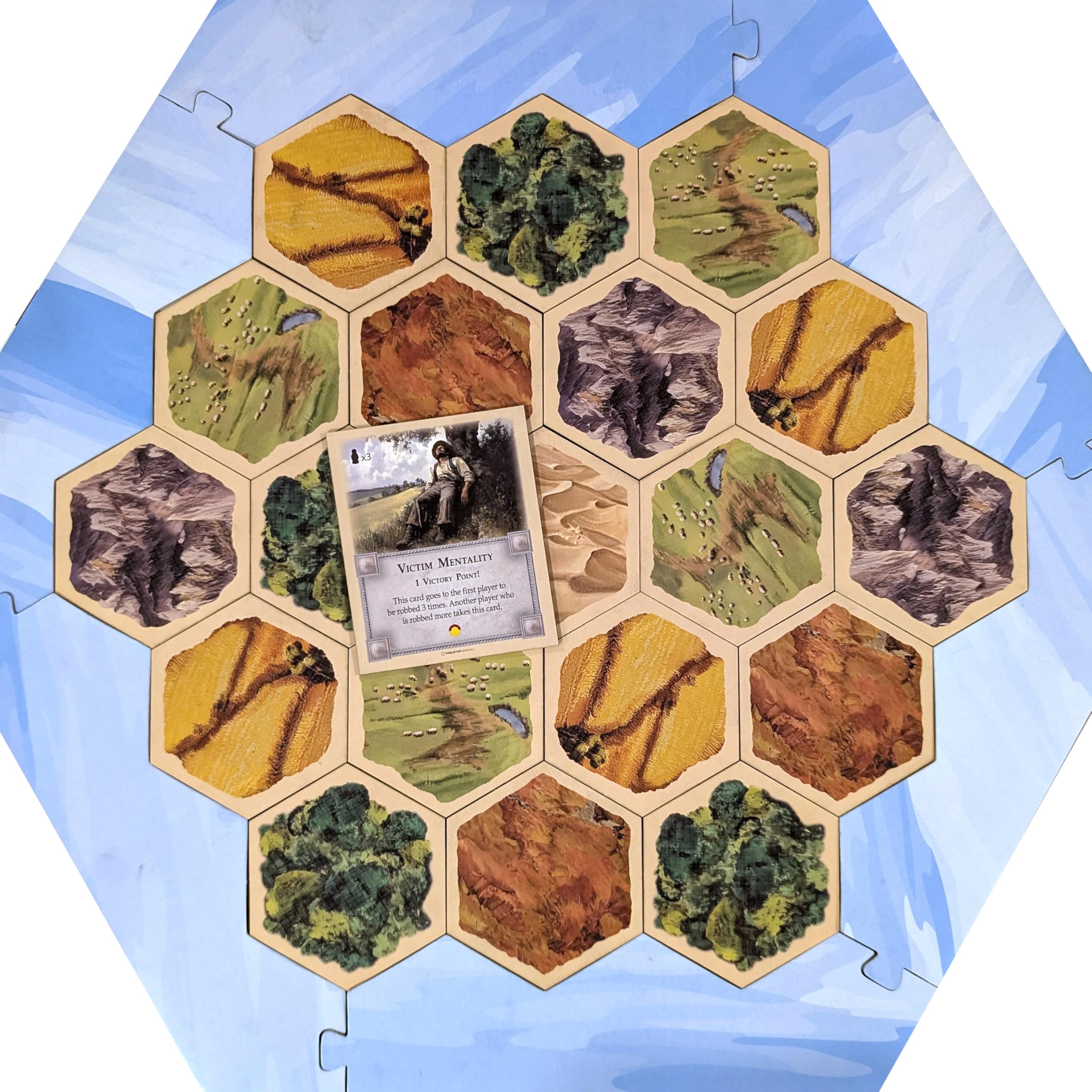 Tabletop Monthly Victim Mentality Card with Catan board, shows matching thickness and fit.