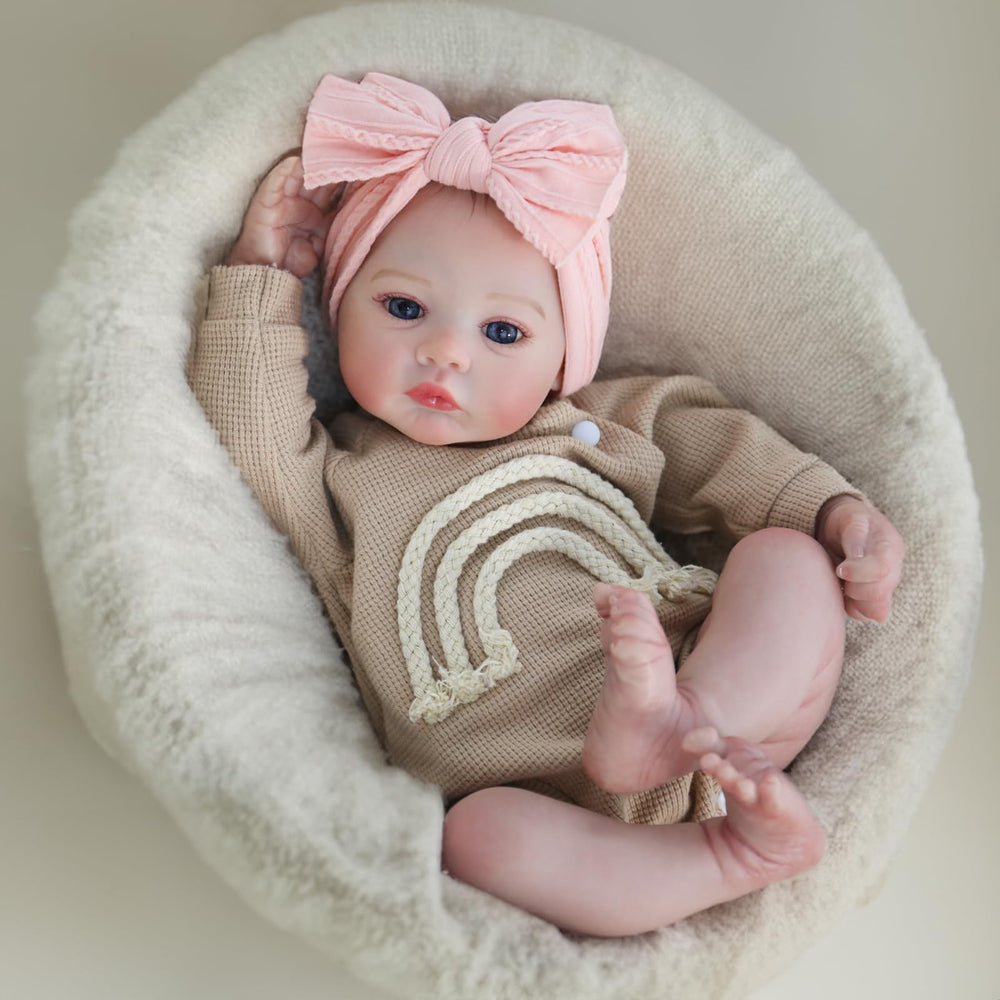 Tan knit outfit with rainbow stripes and pink bow on the doll's head